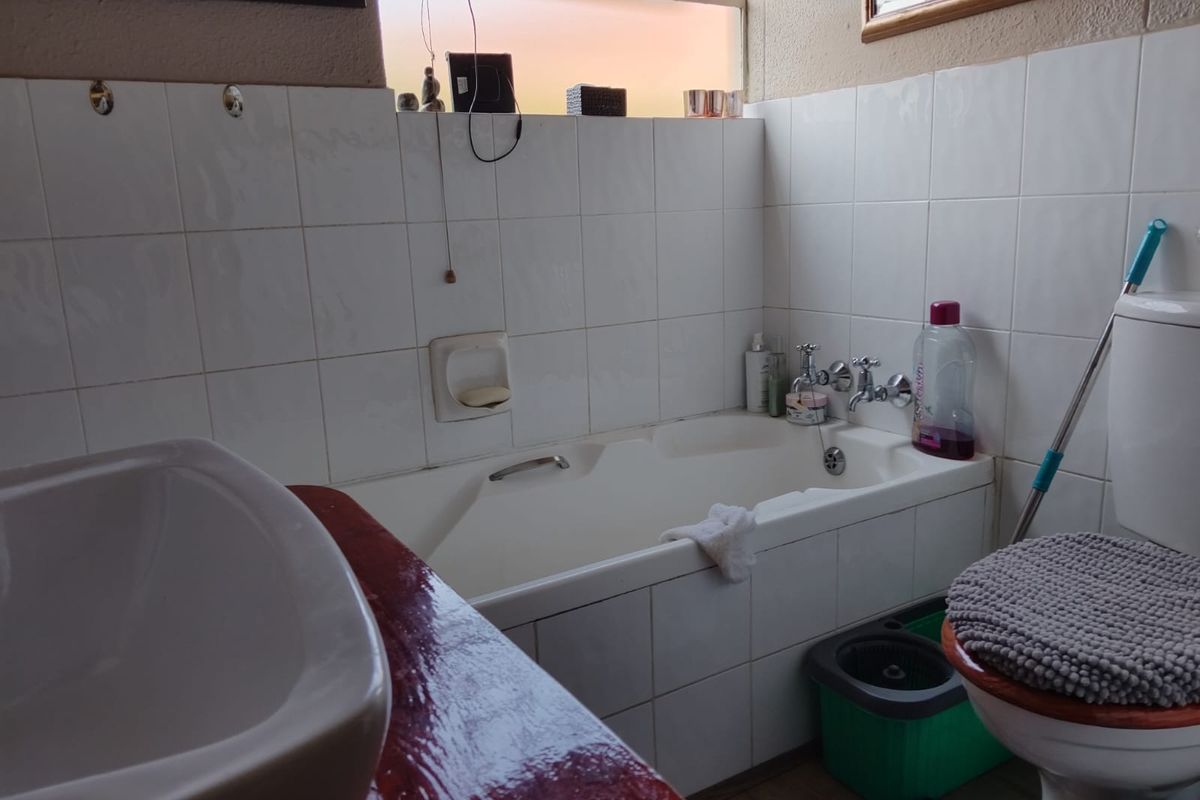 A functional bathroom featuring a built-in bathtub, tiled walls, a vanity basin, and a standard toilet.