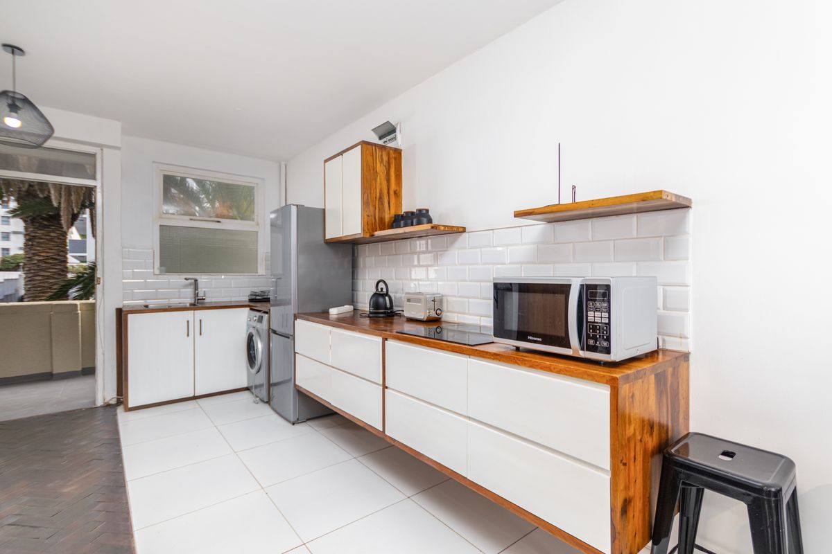 Modern kitchen featuring white cabinetry, wooden countertops, subway tile backsplash, and integrated laundry plumbing, with direct access to an outdoor balcony area.