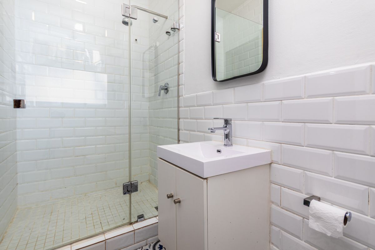 A compact bathroom featuring a glass-enclosed shower, white subway tile wall cladding, and a modern vanity basin.