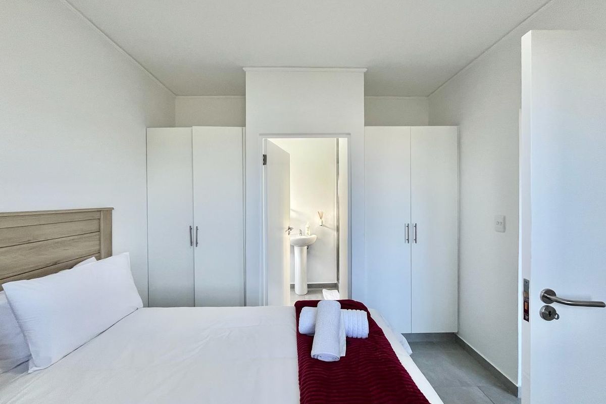 A bright bedroom featuring built-in white cabinetry and an en-suite bathroom with a pedestal sink.