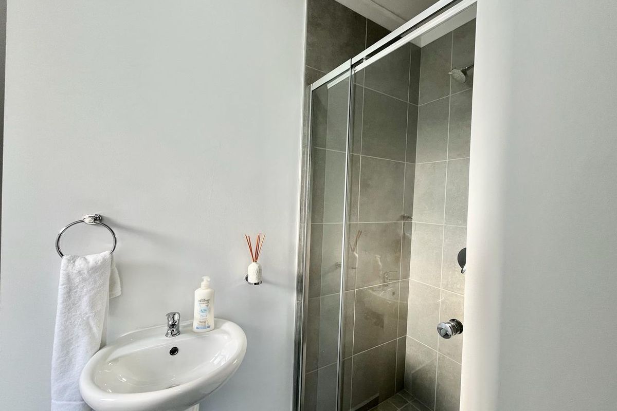 A modern bathroom featuring a pedestal sink, chrome towel ring, and a glass-enclosed shower with neutral grey wall and floor tiling.