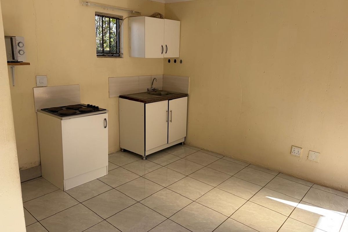 A compact kitchen area featuring basic cabinetry, a small sink, and a built-in electric hob with tiled flooring.