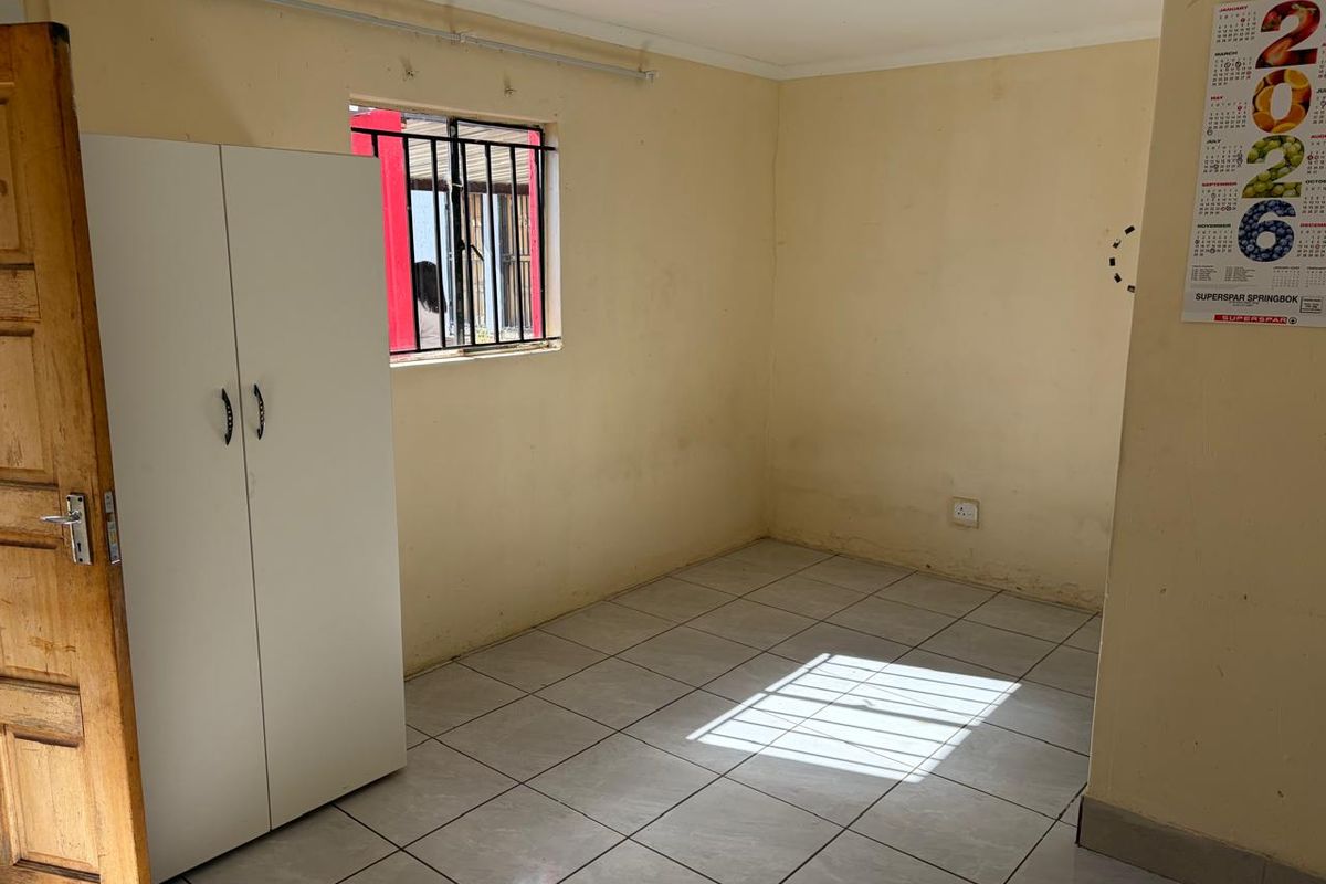 A simple bedroom featuring tiled flooring, a window with security bars, and neutral wall finishes, offering a blank canvas for potential updates.
