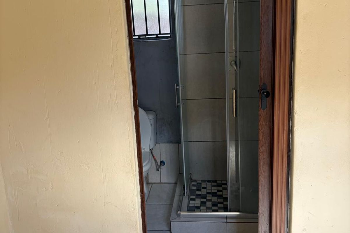 A compact bathroom featuring a glass-enclosed shower, toilet, and tiled flooring, accessible through a doorway from the adjacent room.