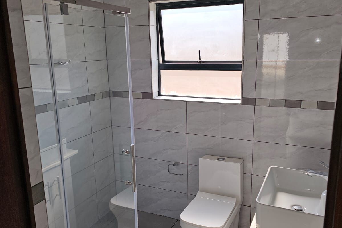 Modern bathroom featuring a glass-enclosed shower, contemporary toilet, and a vanity basin with full-height wall tiling.