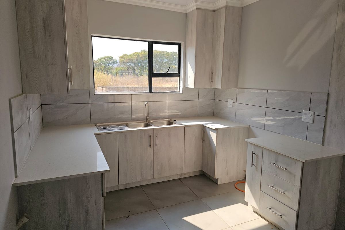 A modern kitchen featuring light wood-grain cabinetry, stone-look countertops, tiled splashbacks, and a double-basin sink with a window view.
