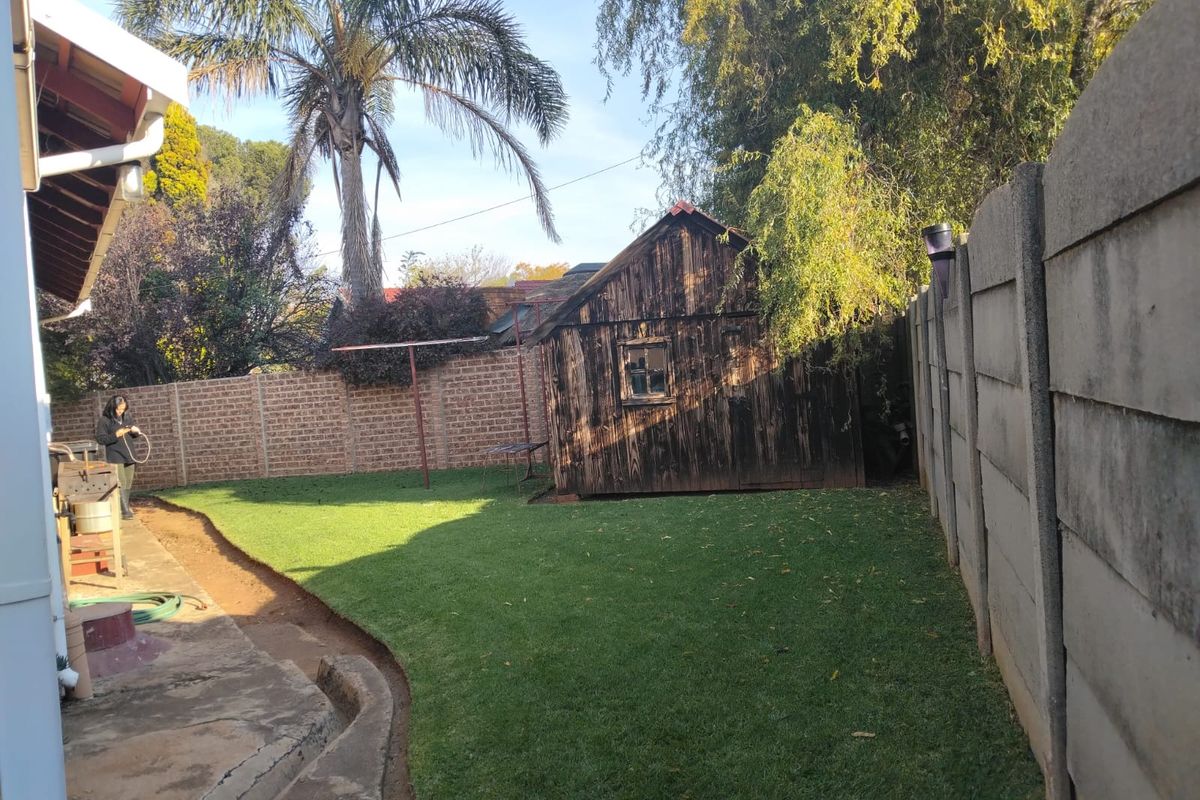 A private rear garden featuring a lawn, concrete patio area, and a detached timber storage shed enclosed by perimeter boundary walls.
