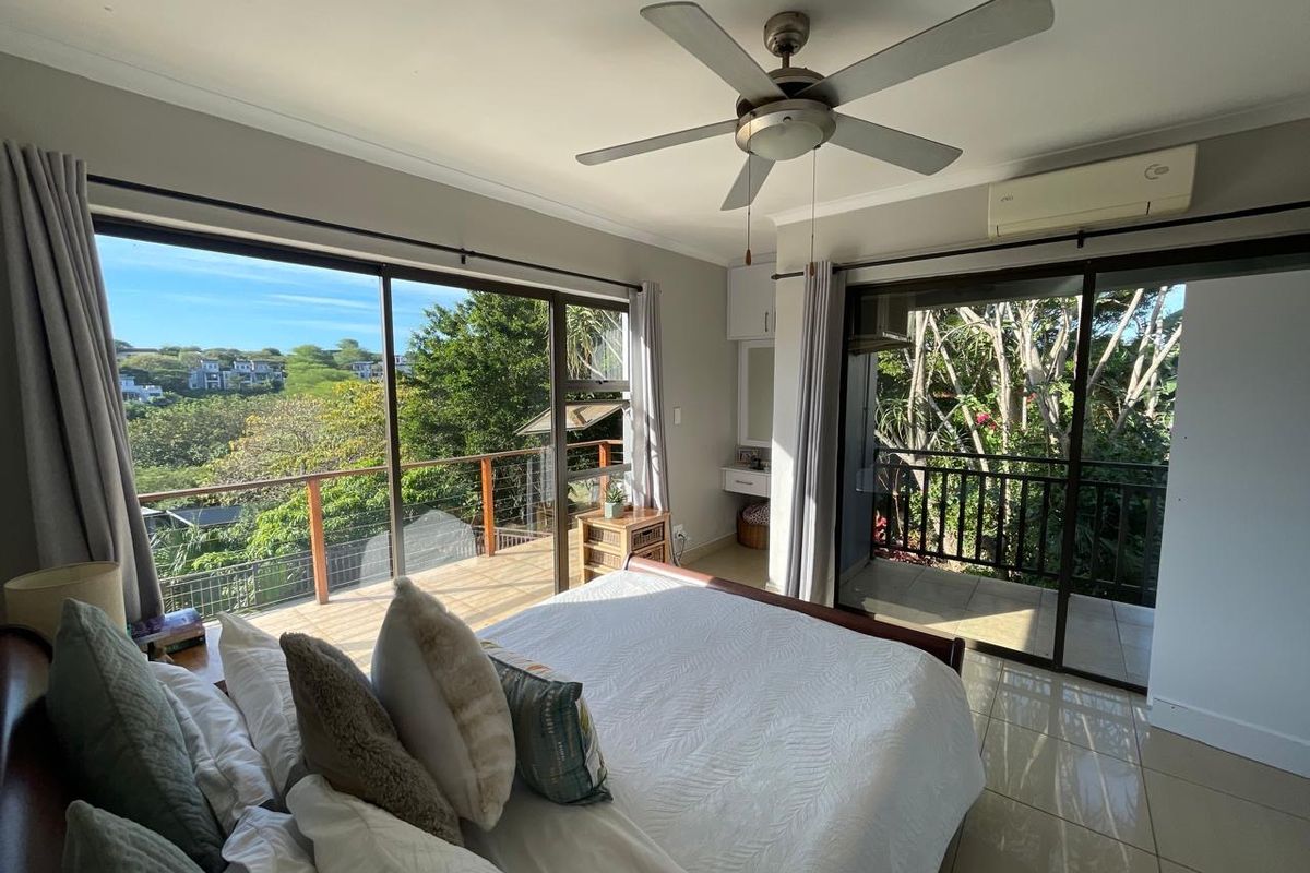 Spacious bedroom featuring large sliding glass doors that open onto a private balcony with scenic views, complemented by a ceiling fan and air conditioning.