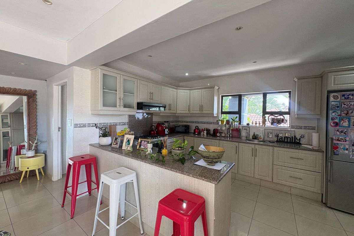A functional kitchen featuring light-toned cabinetry, granite countertops, a breakfast bar, and tiled flooring, integrated into an open-plan living space.