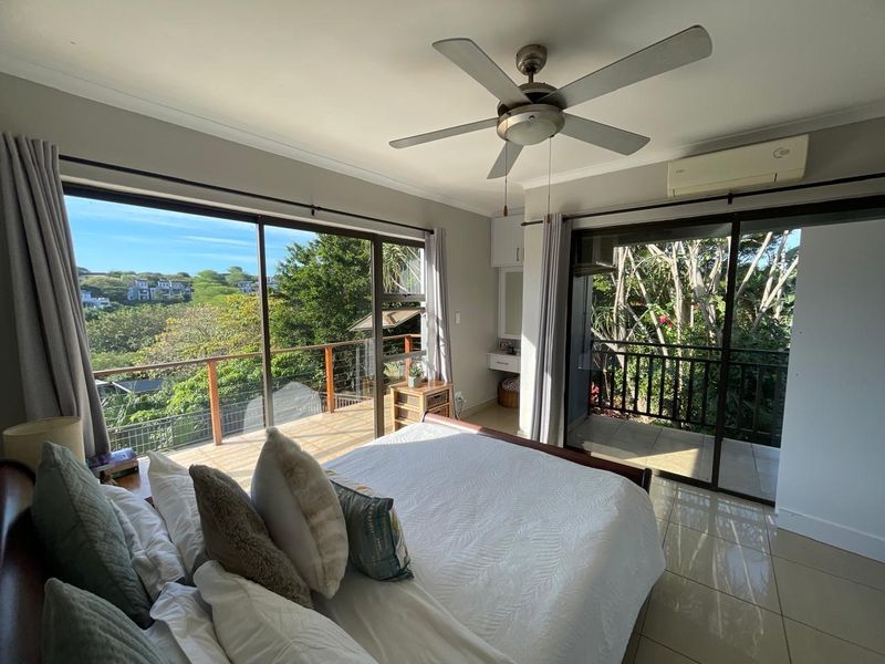 Spacious bedroom featuring large sliding glass doors that open onto a private balcony with scenic views, complemented by a ceiling fan and air conditioning.