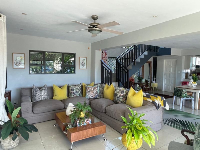 An open-plan living area featuring tiled flooring, a ceiling fan, and a staircase leading to the upper level.