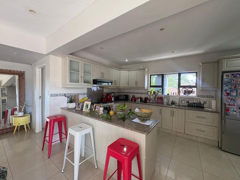A functional kitchen featuring light-toned cabinetry, granite countertops, a breakfast bar, and tiled flooring, integrated into an open-plan living space.