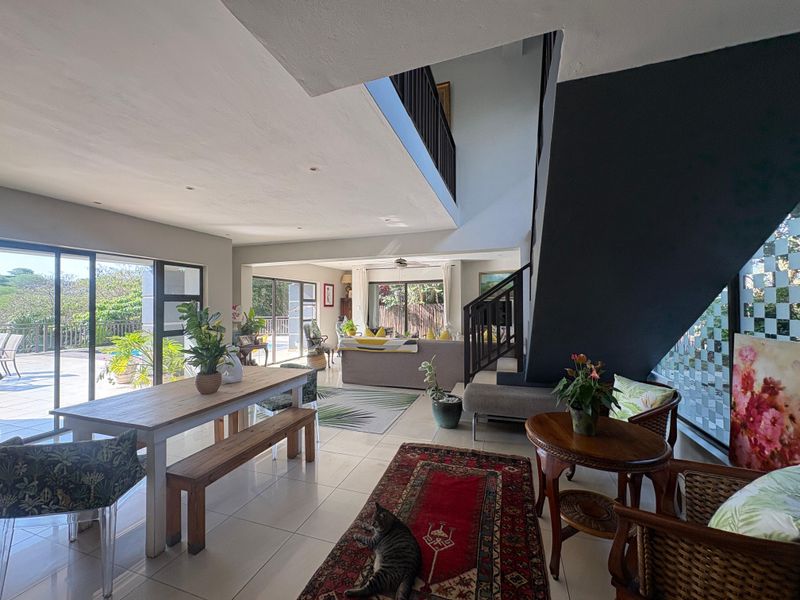 Spacious open-plan living and dining area featuring large sliding glass doors, tiled flooring, and a central staircase leading to the upper level.