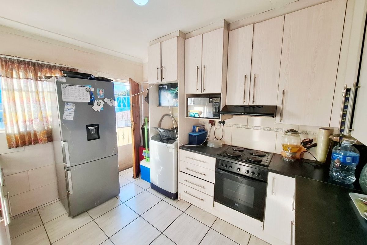 A functional kitchen featuring light-toned built-in cabinetry, a black countertop, integrated oven and hob, and tiled flooring with direct access to an exterior door.