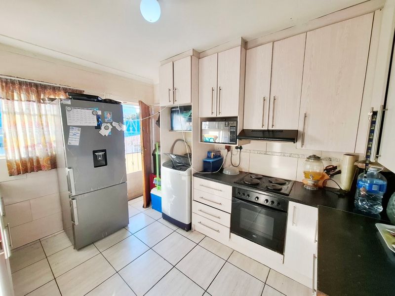 A functional kitchen featuring light-toned built-in cabinetry, a black countertop, integrated oven and hob, and tiled flooring with direct access to an exterior door.