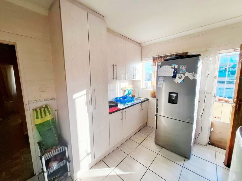A functional kitchen featuring light-toned built-in cabinetry, tiled flooring, and a stainless steel sink with direct access to an outdoor area.