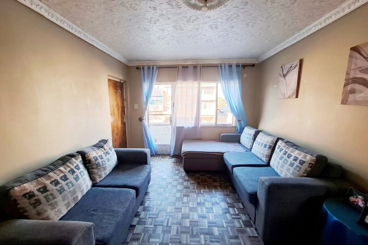 A living room featuring parquet flooring, decorative ceiling coving, and a central ceiling rose, with direct access to a balcony through a sliding door.