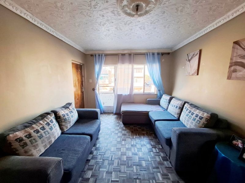 A living room featuring parquet flooring, decorative ceiling coving, and a central ceiling rose, with direct access to a balcony through a sliding door.