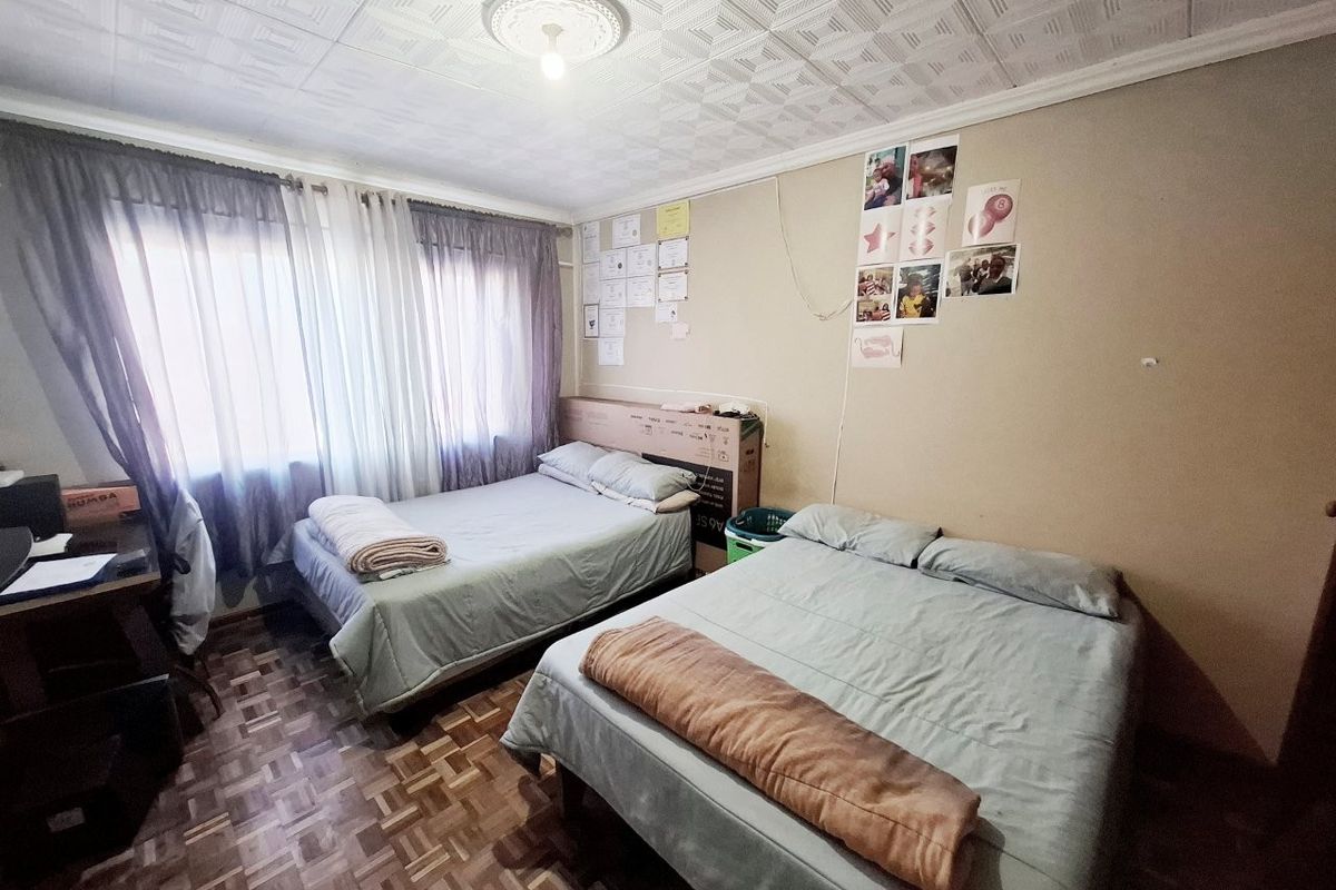 A bedroom featuring parquet flooring and a textured ceiling with a central ceiling rose, offering a functional space with potential for cosmetic updates.