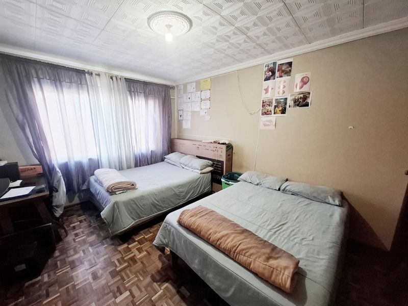 A bedroom featuring parquet flooring and a textured ceiling with a central ceiling rose, offering a functional space with potential for cosmetic updates.