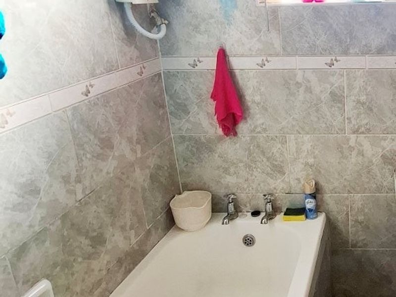 A functional bathroom featuring a standard bathtub, tiled wall finishes, and an exposed electric water heater unit.