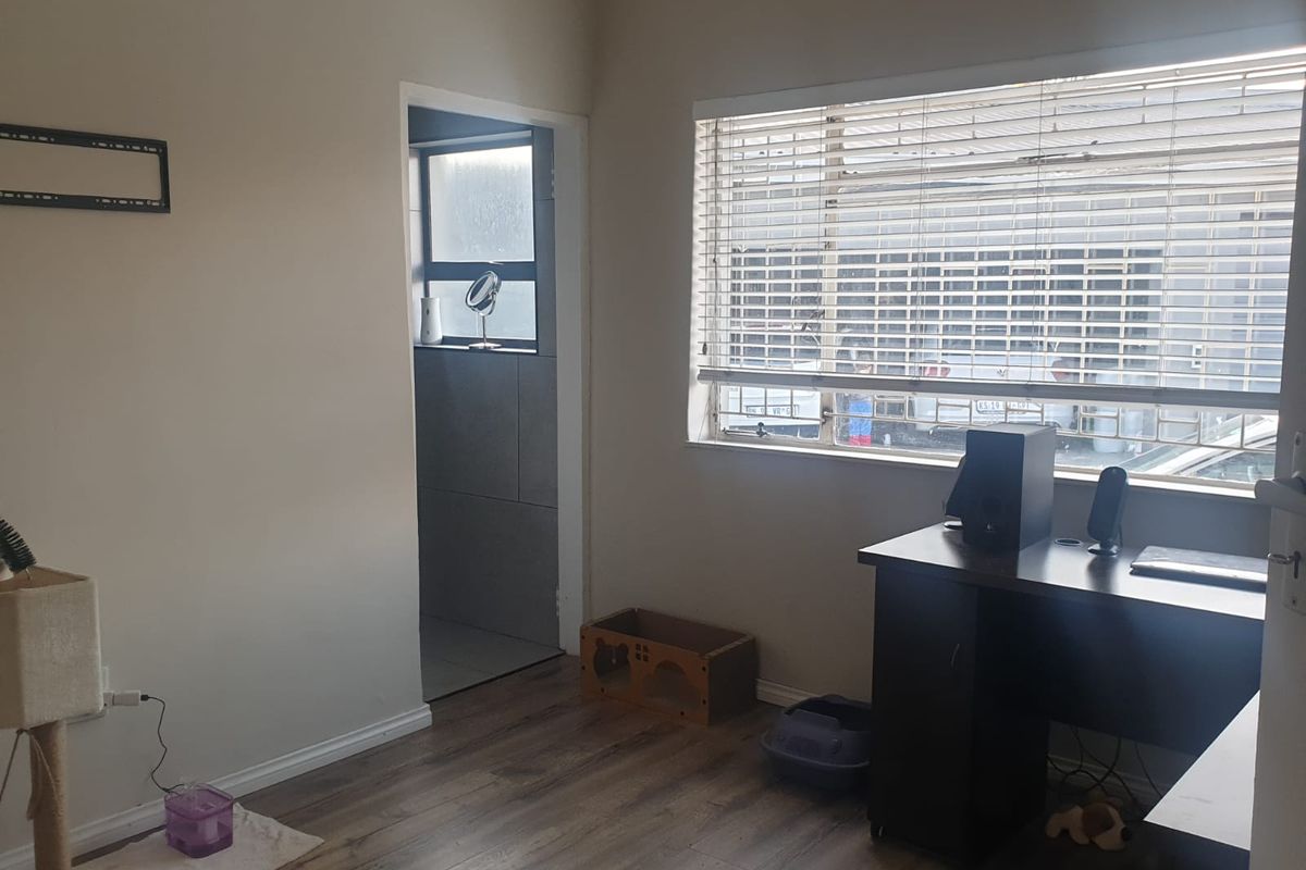A functional bedroom featuring wood-look laminate flooring, horizontal window blinds, and an adjoining en-suite bathroom area.