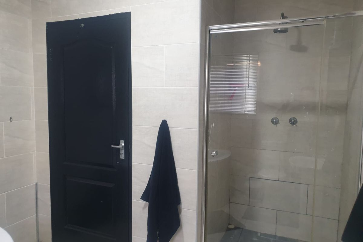 A bathroom featuring light-toned wall tiles, a glass-enclosed shower with a fixed shower head, and a contrasting black door.