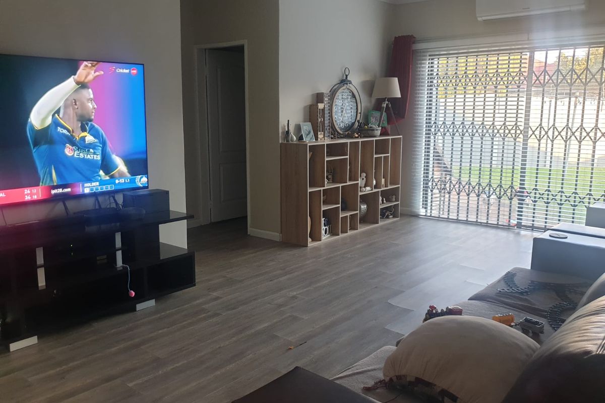 A comfortable living room featuring wood-look laminate flooring, a wall-mounted air conditioning unit, and sliding glass doors with security gates leading outdoors.