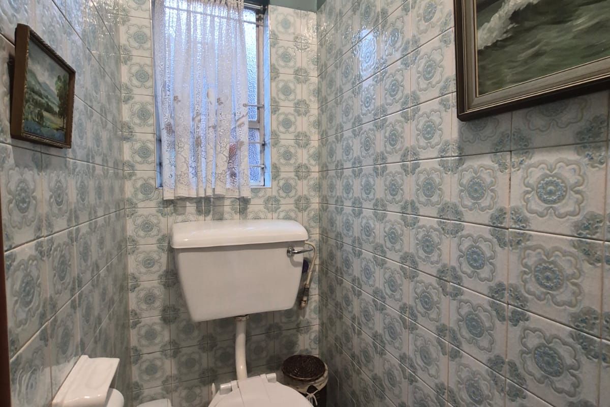 A compact bathroom featuring dated patterned ceramic wall tiles and standard white sanitaryware, offering potential for a modern renovation.