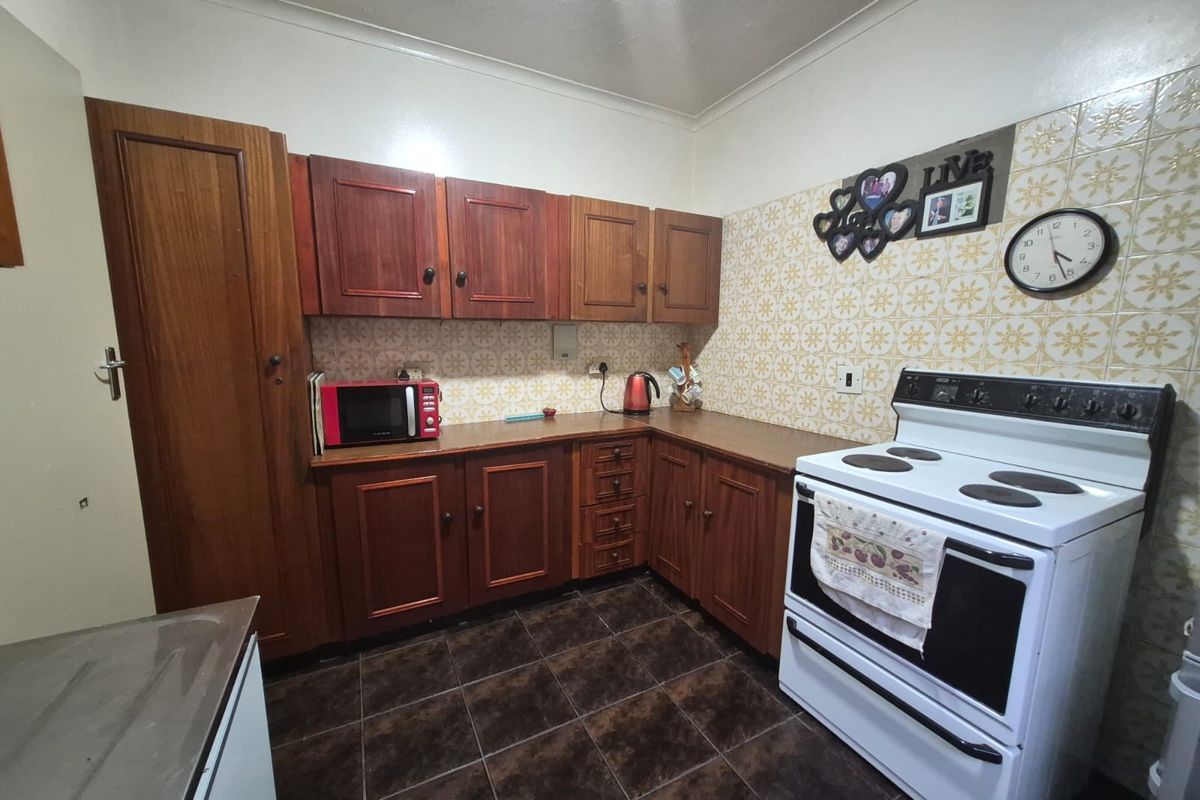 A functional kitchen featuring traditional wooden cabinetry, tiled backsplash, and dark floor tiles, offering a dated aesthetic ready for modernization.