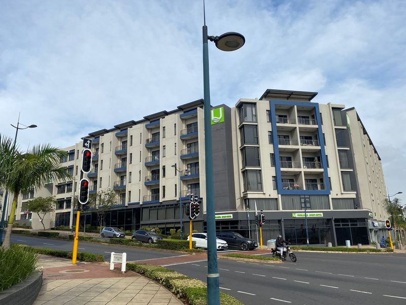 A modern multi-story apartment building featuring contemporary architectural design, private balconies, and ground-floor commercial space, situated on a prominent street corner.