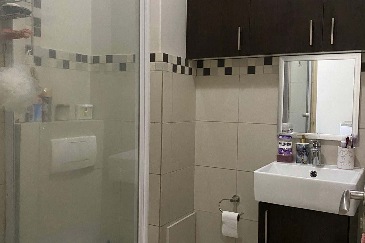 Compact bathroom featuring a wall-mounted vanity, dark cabinetry, a glass-enclosed shower, and neutral wall tiling.