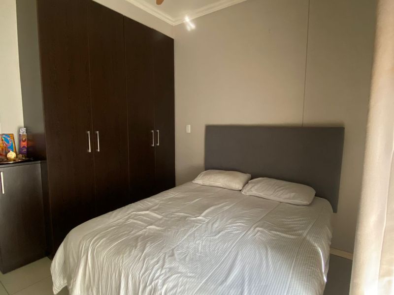 A well-maintained bedroom featuring built-in dark wood cabinetry, tiled flooring, and a modern ceiling fan.