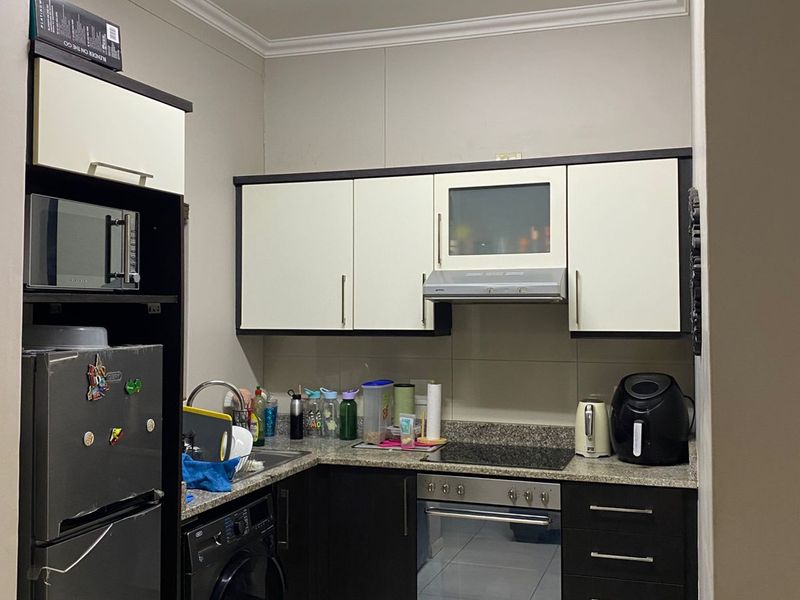 Compact kitchen featuring two-tone cabinetry, granite countertops, built-in oven, hob, extractor fan, and integrated space for a washing machine.