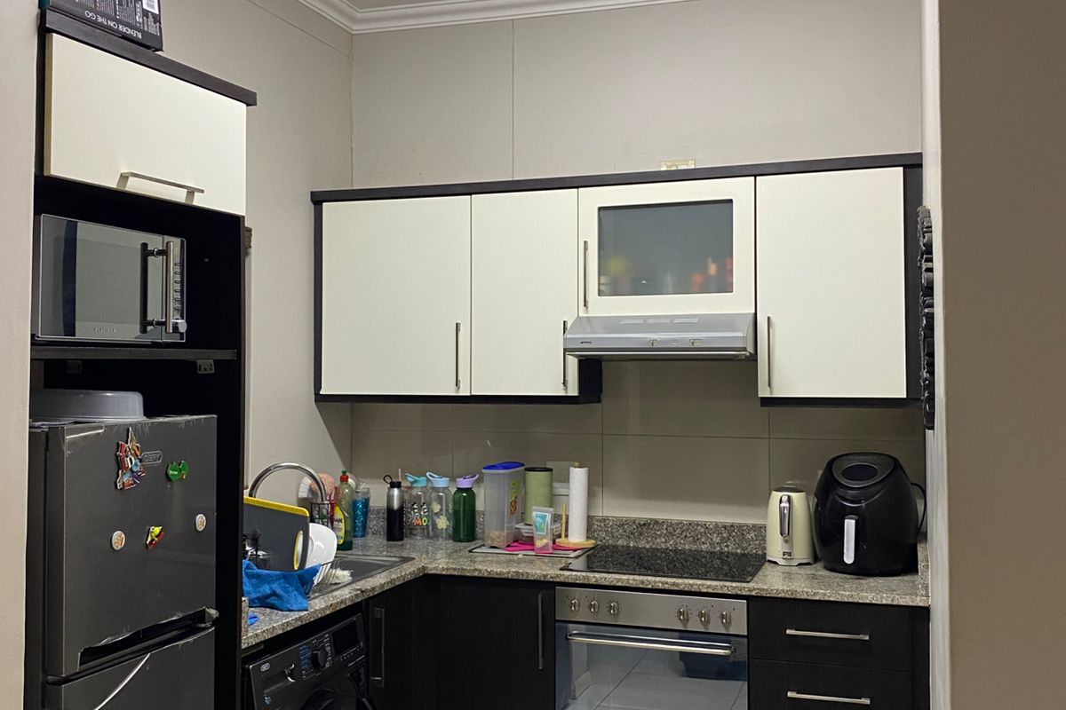 Compact kitchen featuring two-tone cabinetry, granite countertops, built-in oven, hob, extractor fan, and integrated space for a washing machine.