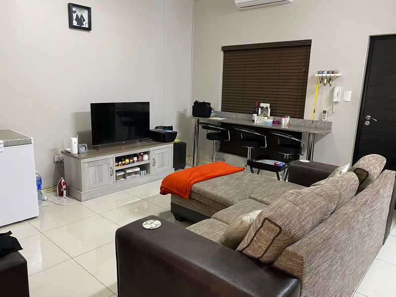 Open plan living area featuring tiled flooring, a built-in breakfast bar with granite countertop, and a wall-mounted air conditioning unit.