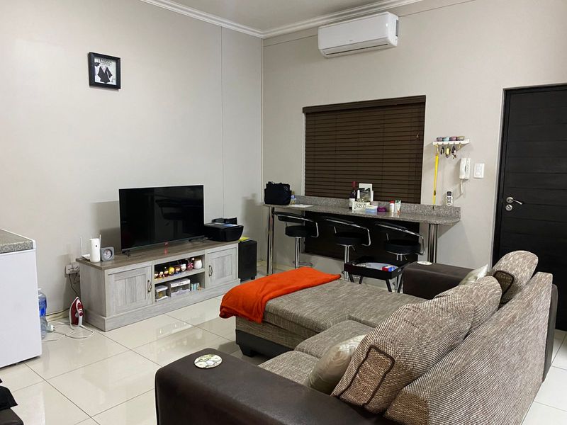 An open-plan living area featuring tiled flooring, a wall-mounted air conditioning unit, and a built-in breakfast bar with integrated seating.