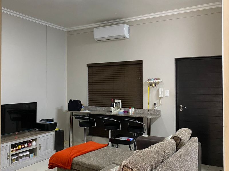 A well-maintained open-plan living area featuring tiled flooring, a wall-mounted air conditioning unit, and a built-in breakfast bar with granite countertop.