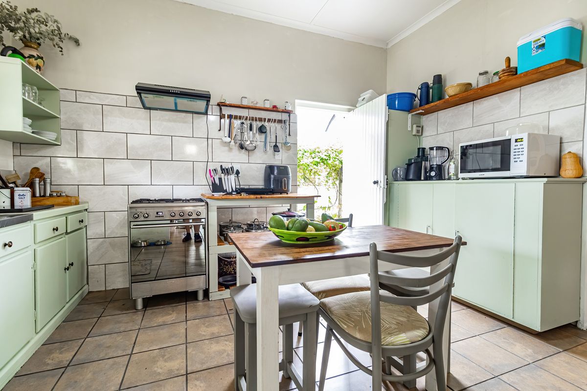 A functional kitchen featuring light green cabinetry, tiled splashbacks, a gas stove with extractor fan, and direct access to the outdoor area.