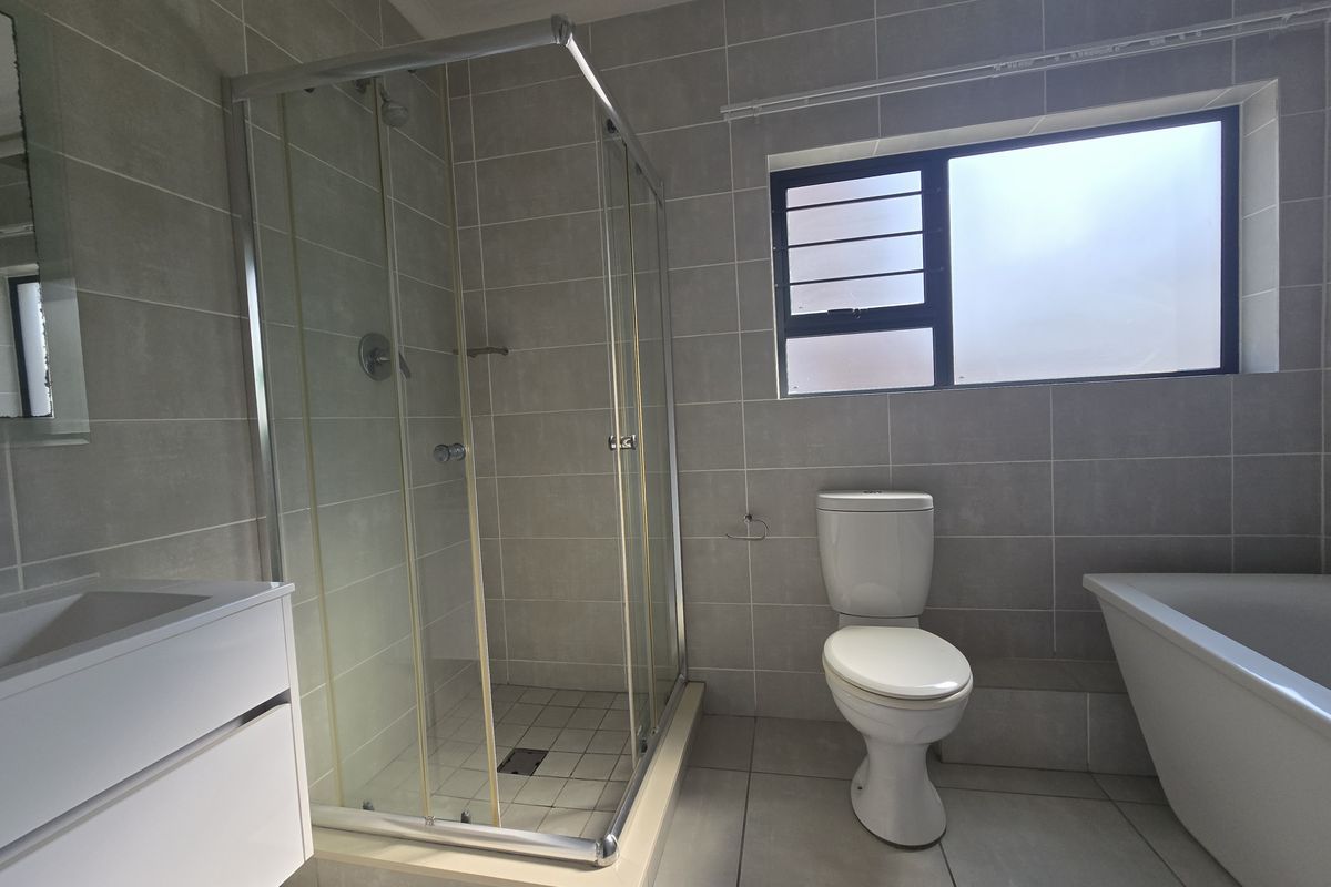 Modern bathroom featuring a glass-enclosed shower, a separate bathtub, a wall-mounted vanity, and neutral floor-to-ceiling tiling.
