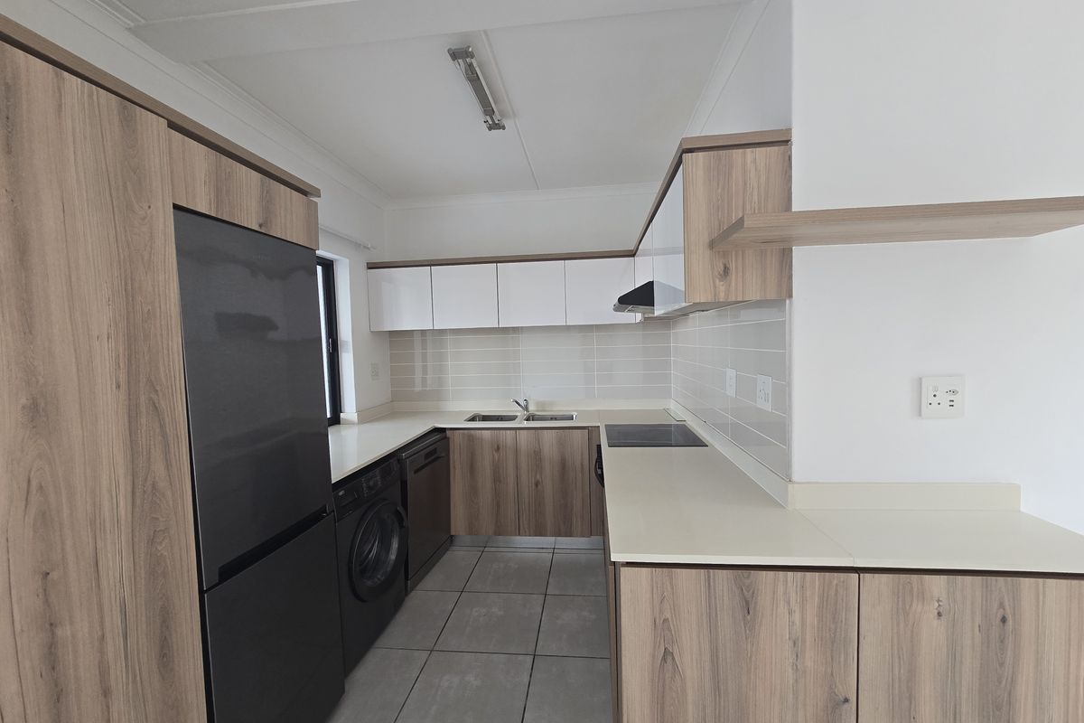 Modern kitchen featuring wood-grain cabinetry, light-toned countertops, tiled backsplash, integrated hob, and dedicated space for laundry appliances.