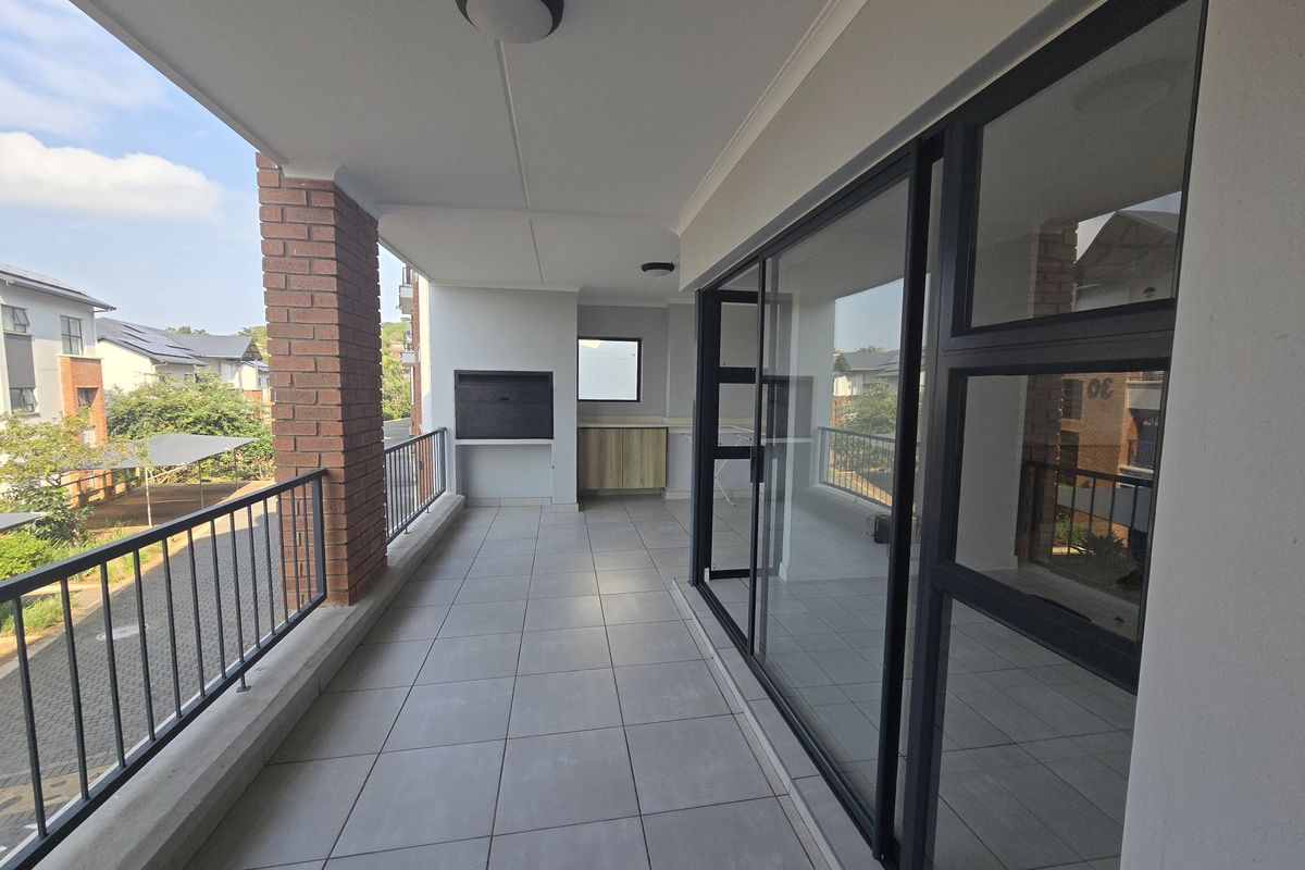 A spacious covered balcony featuring tiled flooring, a built-in braai, and large sliding glass doors providing seamless access to the interior living space.