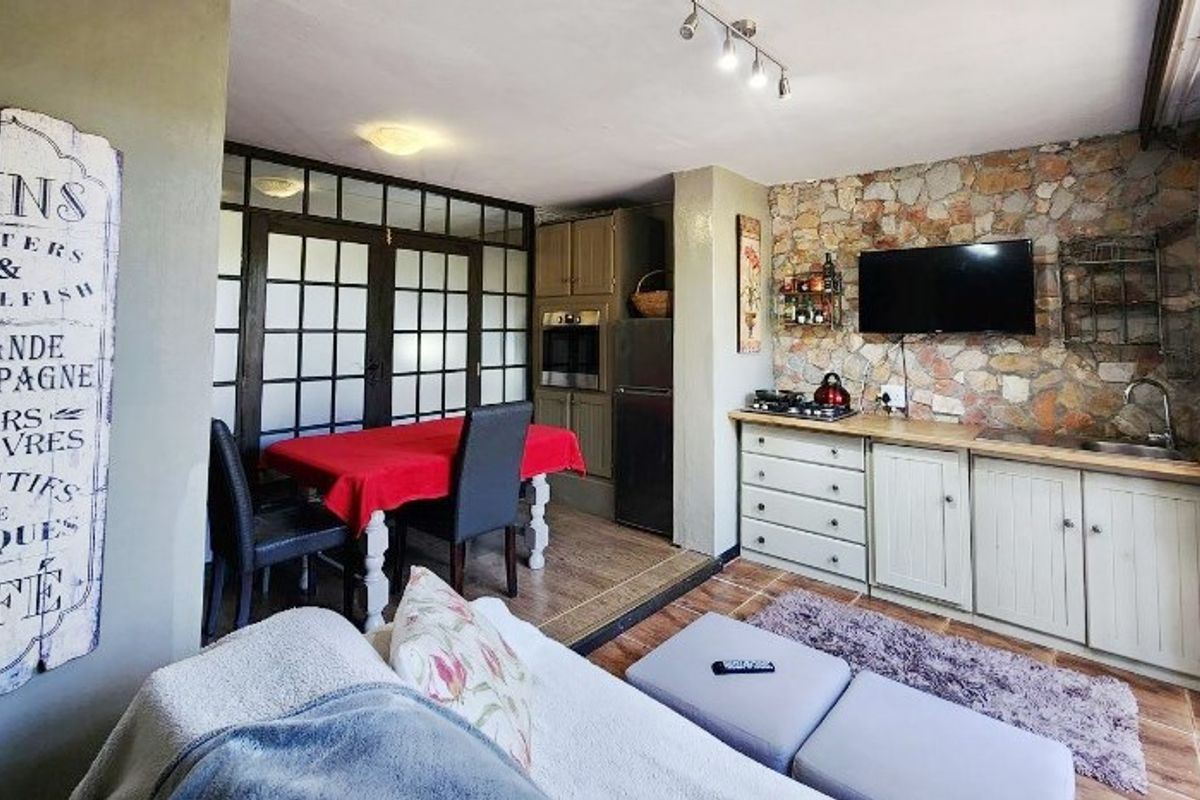 Open-plan living and kitchen area featuring a rustic stone accent wall, built-in cabinetry, integrated oven, and tiled flooring with access through glass-paned doors.