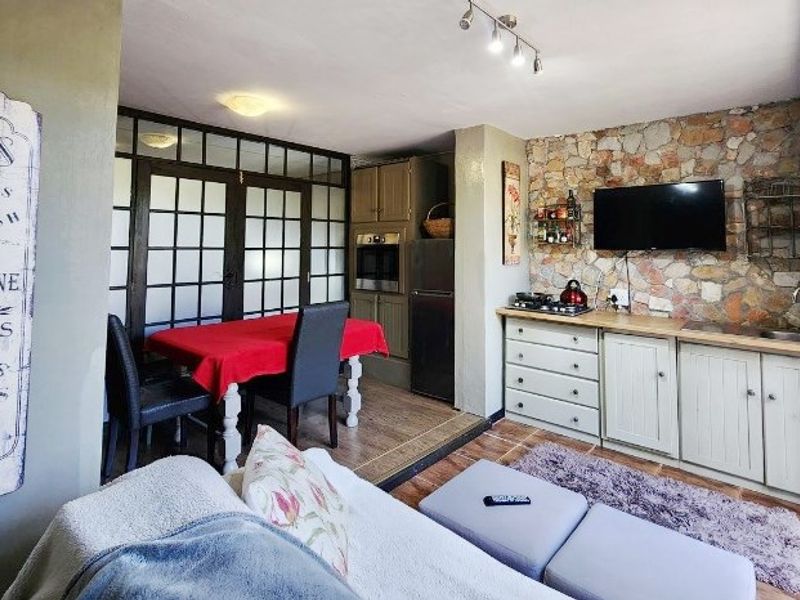 Open-plan living and kitchen area featuring a rustic stone accent wall, built-in cabinetry, integrated oven, and tiled flooring with access through glass-paned doors.