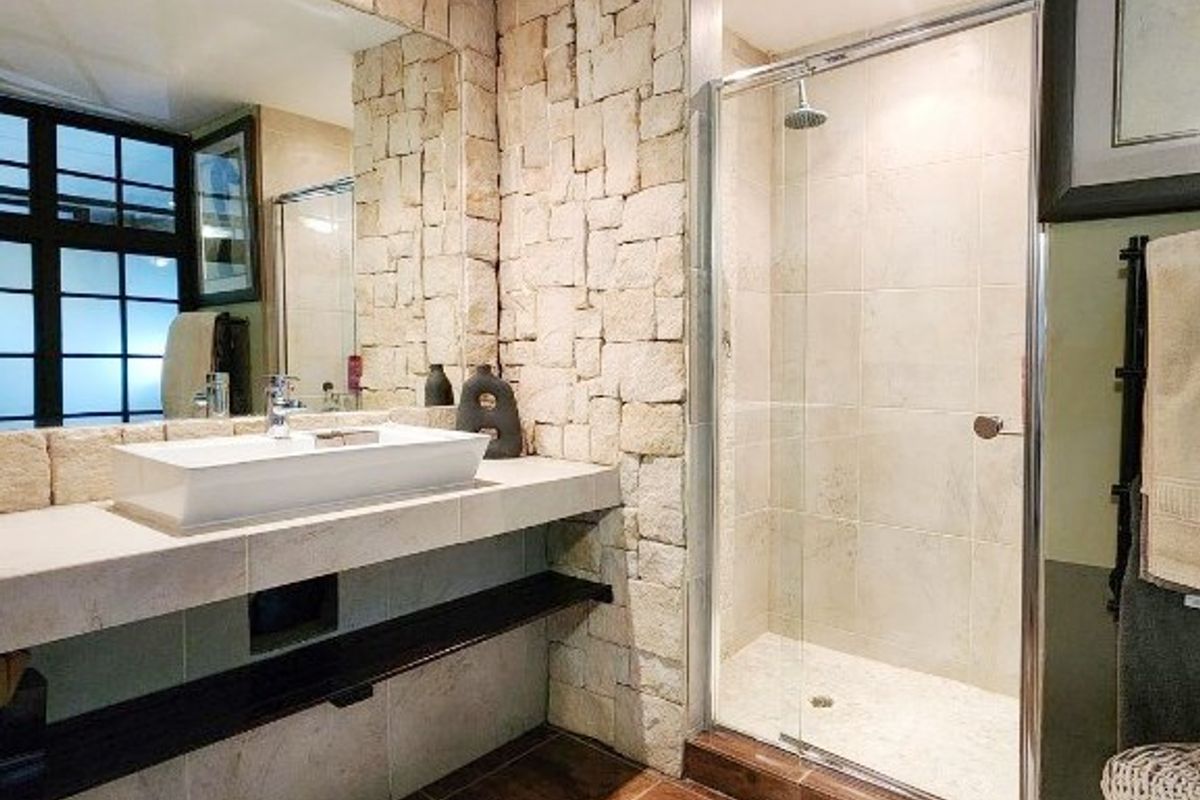 Modern bathroom featuring a stone accent wall, floating vanity with a vessel sink, and a glass-enclosed shower with tiled finishes.
