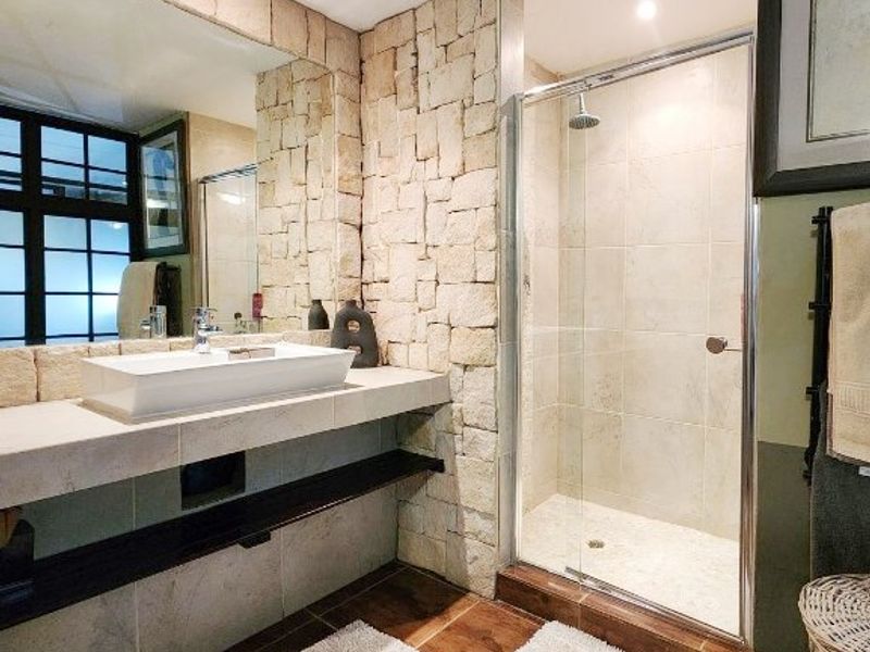 Modern bathroom featuring a stone accent wall, floating vanity with a vessel sink, and a glass-enclosed shower with tiled finishes.