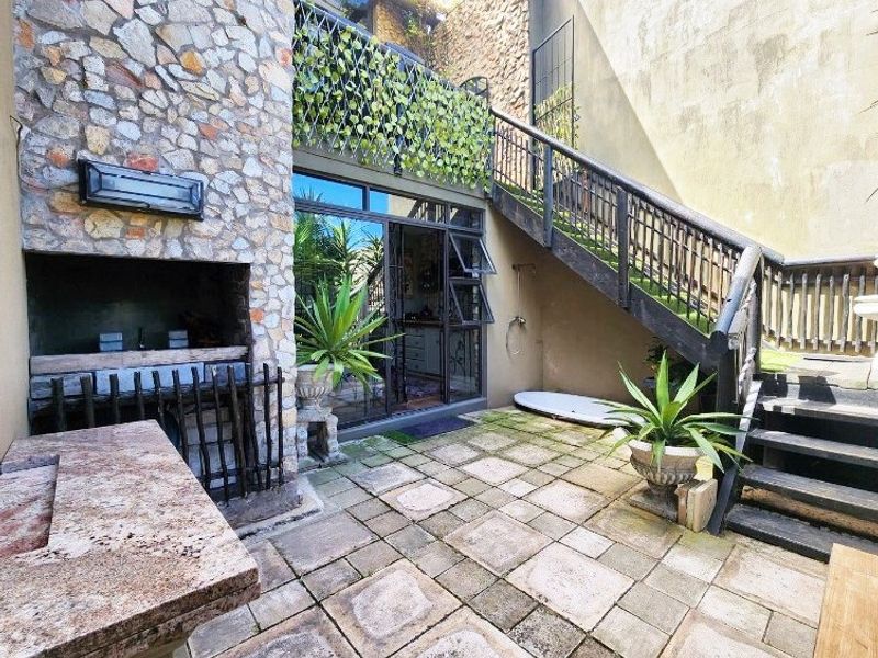 Outdoor patio area featuring a stone-clad built-in braai, granite prep surface, and a metal staircase leading to an upper level.