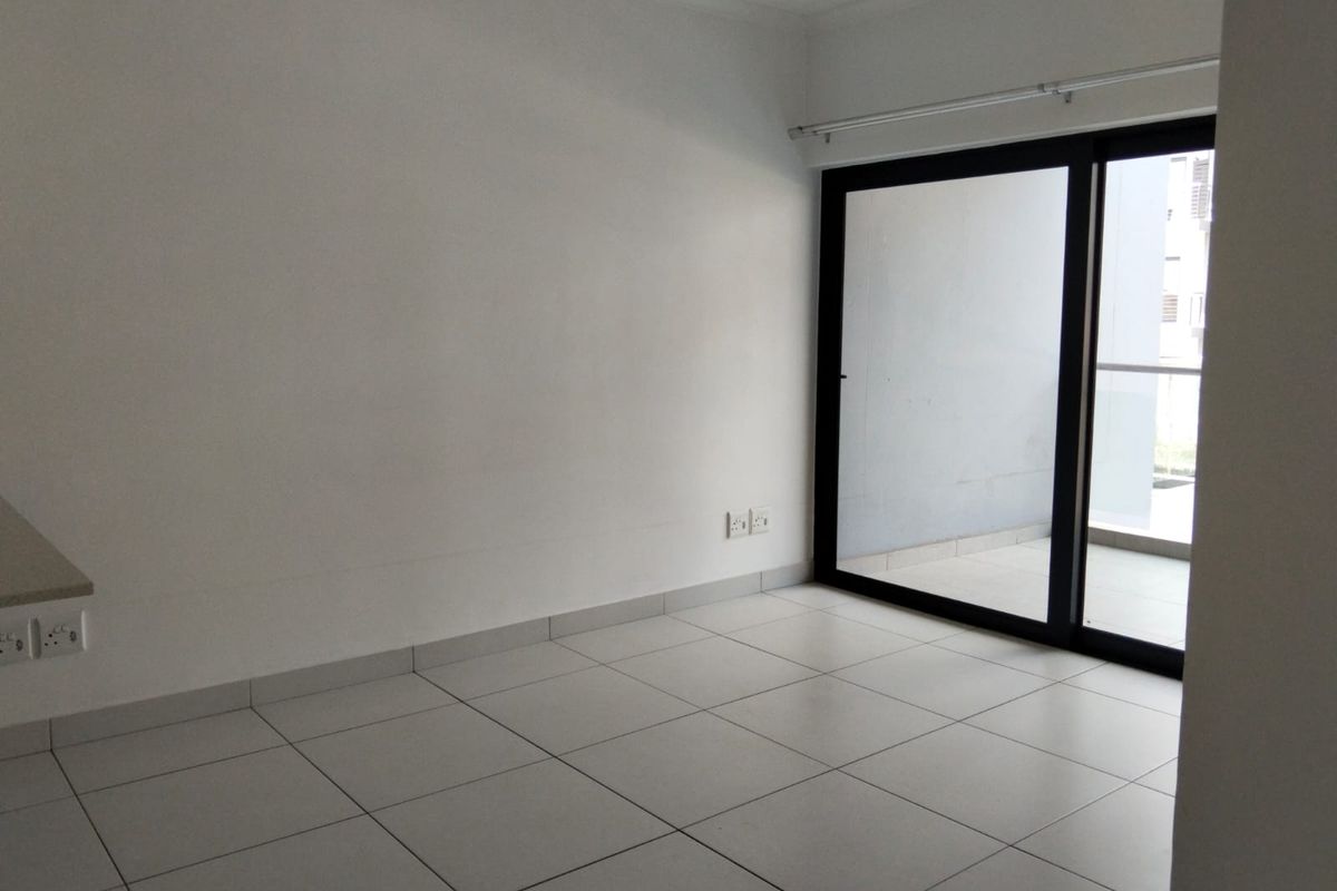A bright, empty living area featuring neutral floor tiles and large sliding glass doors that provide direct access to an outdoor balcony.