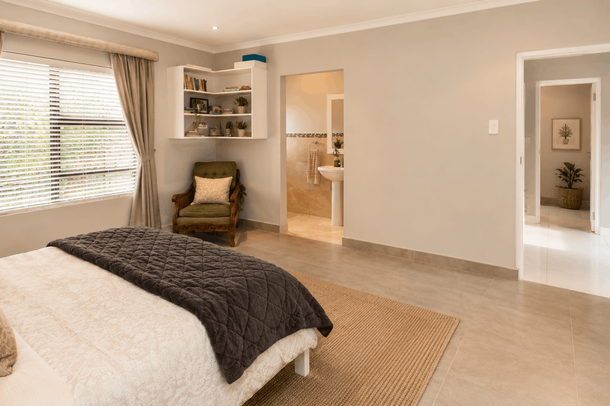 Spacious bedroom featuring neutral tiled flooring, built-in corner shelving, and an en-suite bathroom, with direct access to the hallway.