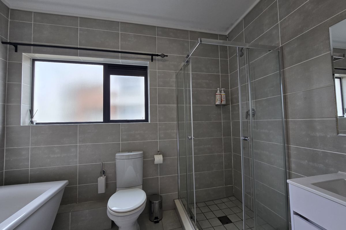 Modern bathroom featuring a freestanding bathtub, glass-enclosed shower, toilet, and vanity with neutral grey wall tiles and tiled flooring.